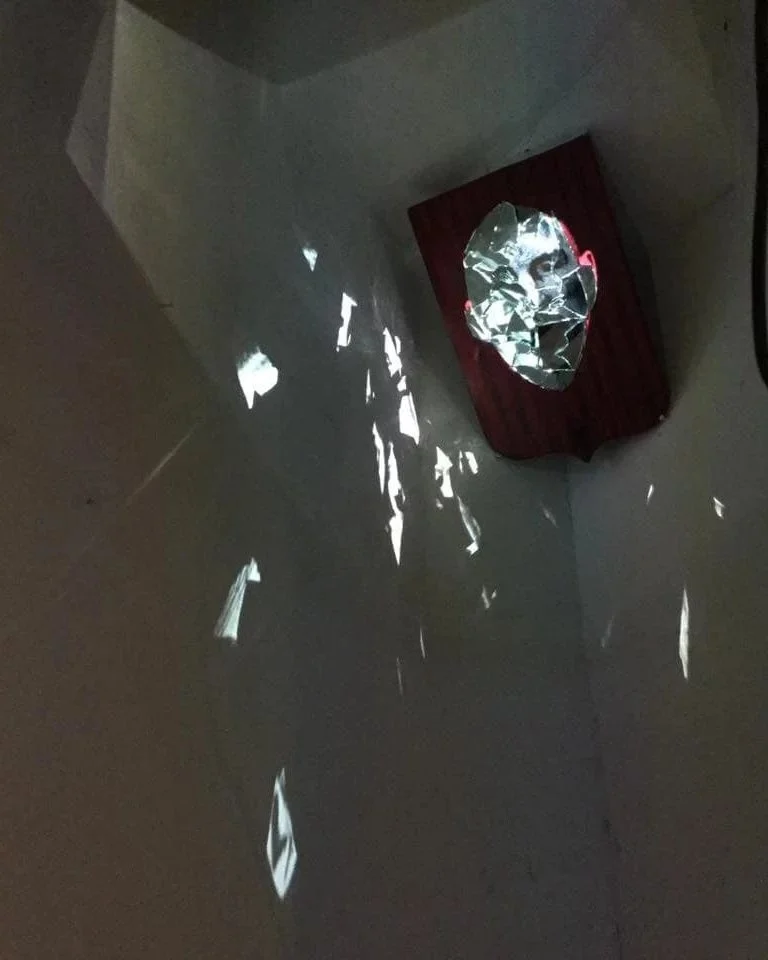 Video projected onto the mirror face, reflections scattered across the walls